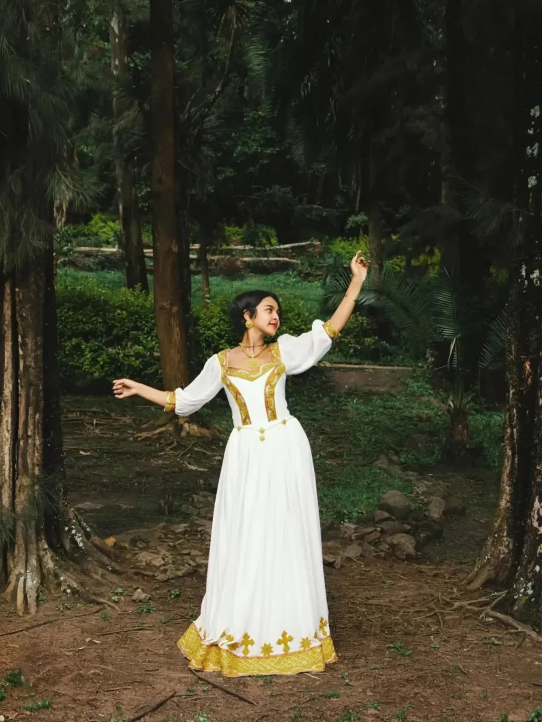 Woman in a white and gold dress standing in a forest. Gold Zuria Habesha Kemis Modern Ethiopian Traditional Dress ethgebya gebeya usa habesha kemis