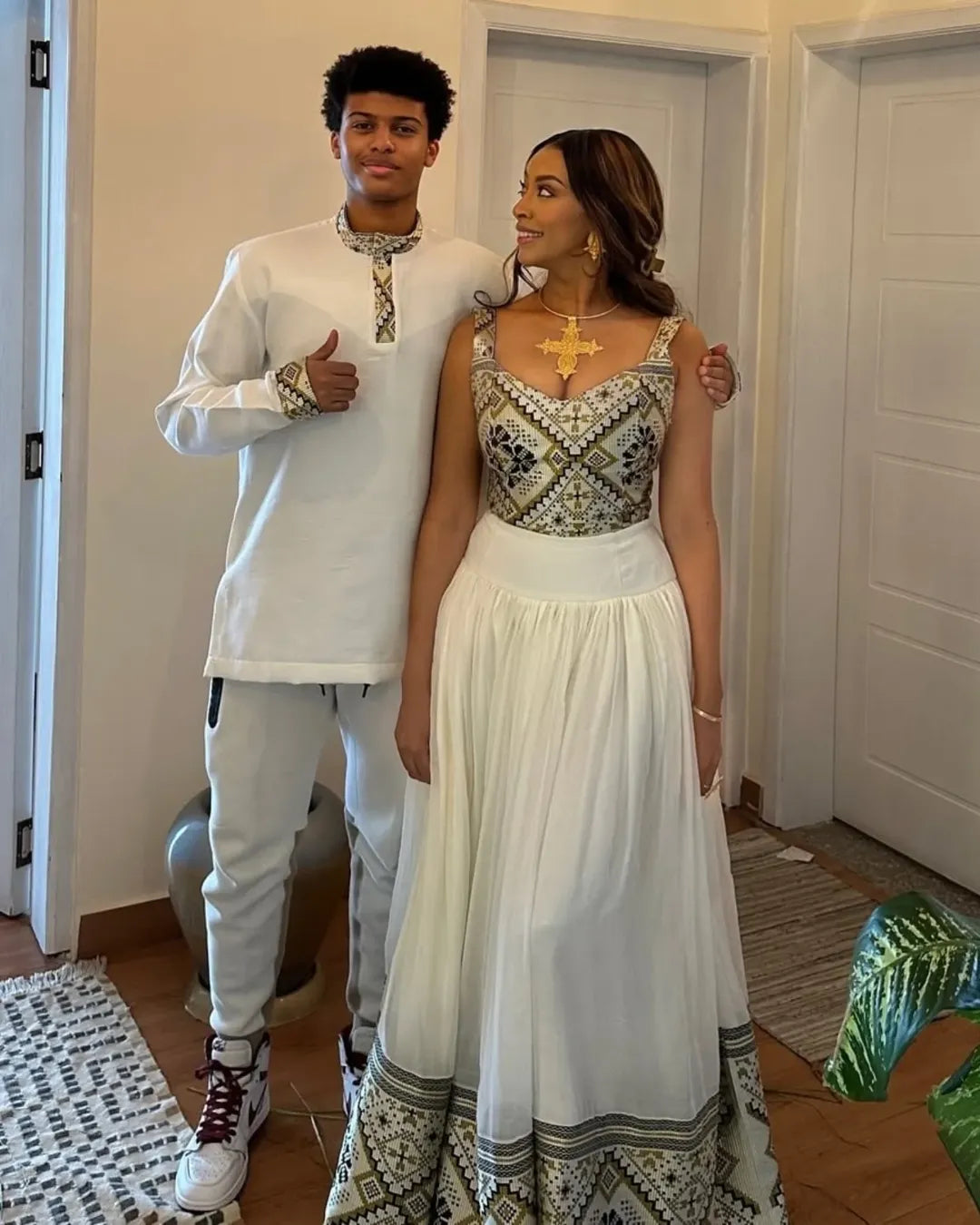 Two people standing indoors, one in a white outfit and the other in a patterned dress. Luxury Ethiopian Habesha Couple Outfit Matching Modern Attire Set ethiopia gebeya ethgebya