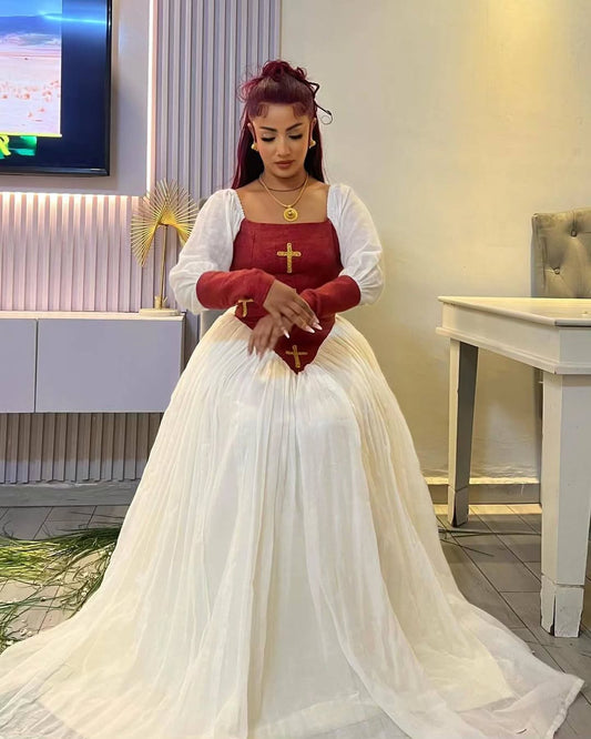 Woman in a red top and white skirt with a long train, holding a red box in a room. Elegant  Modern Red-Accent Habesha Kemis Ethgebya