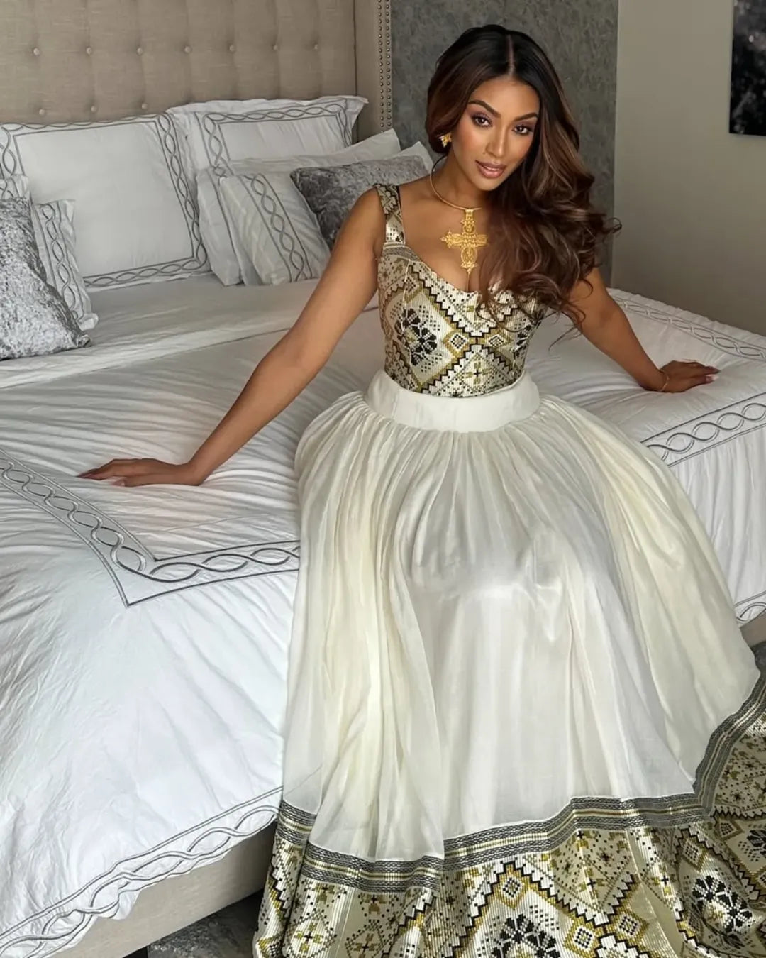 Woman in a patterned dress sitting on a bed with decorative pillows. LuxuryEthiopian Habesha Couple Outfit Matching Modern Attire Set ethiopia gebeya ethgebya
