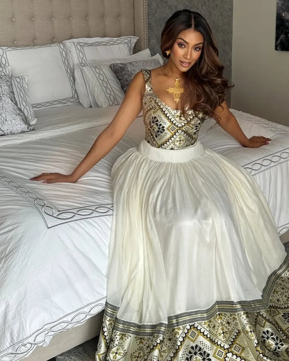 Woman in a patterned dress sitting on a bed with decorative pillows. LuxuryEthiopian Habesha Couple Outfit Matching Modern Attire Set ethiopia gebeya ethgebya