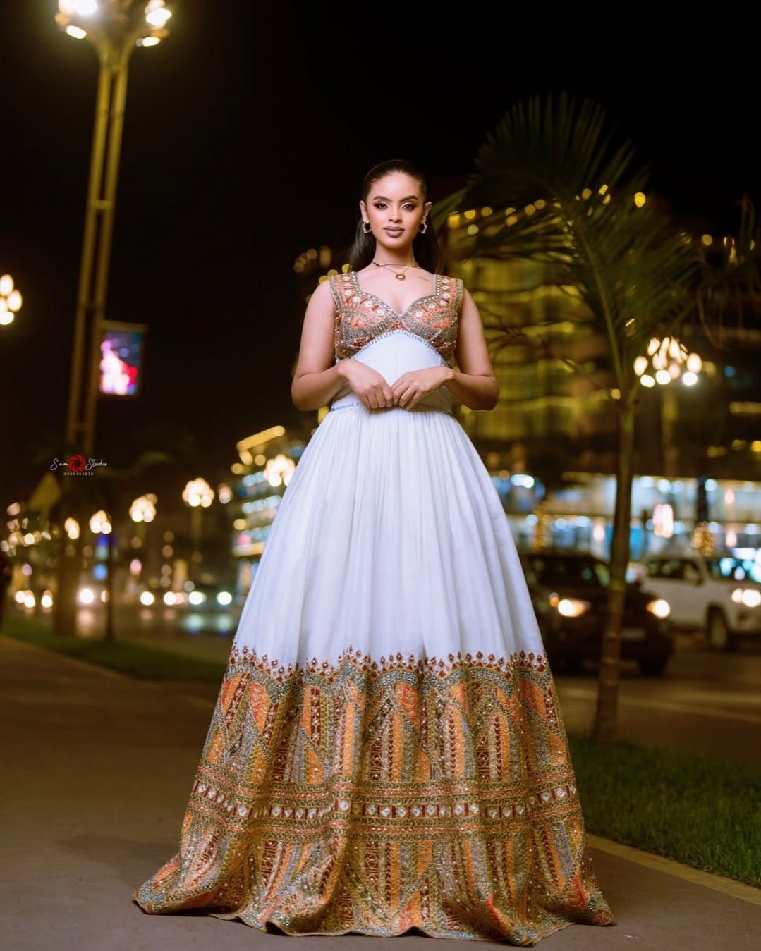 Woman in a white and patterned dress standing on a street at night.