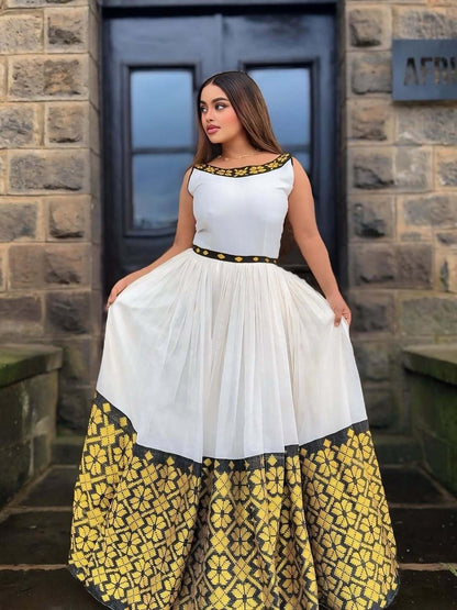 Woman wearing a white top with black and gold accents and a yellow floral skirt in front of a stone building.