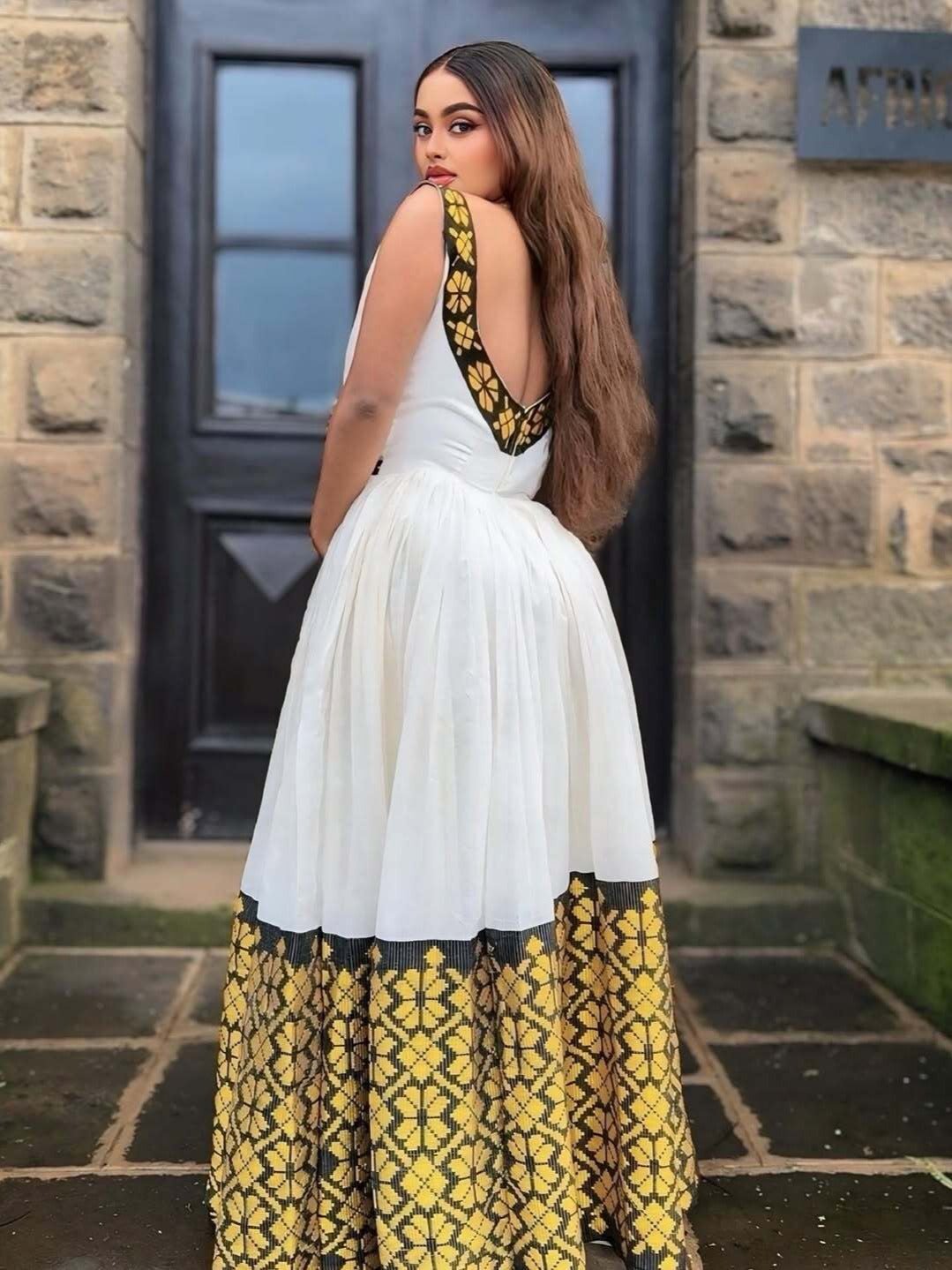 Woman wearing a white dress with yellow and black floral patterns standing in front of a stone building.