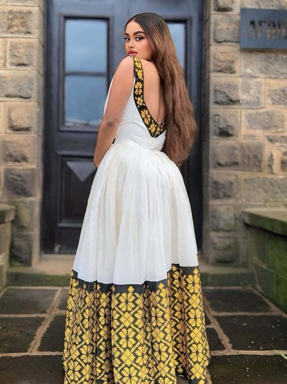 Woman wearing a white dress with yellow and black floral patterns standing in front of a stone building.