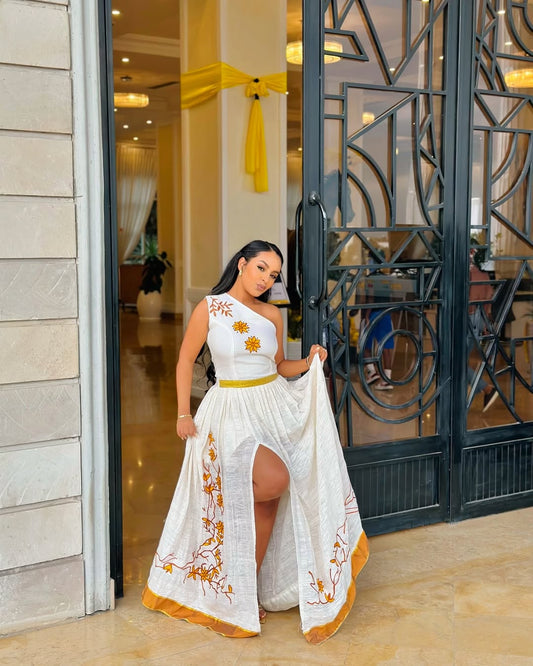 Woman in a white dress with floral patterns standing in front of a decorative metal gate.