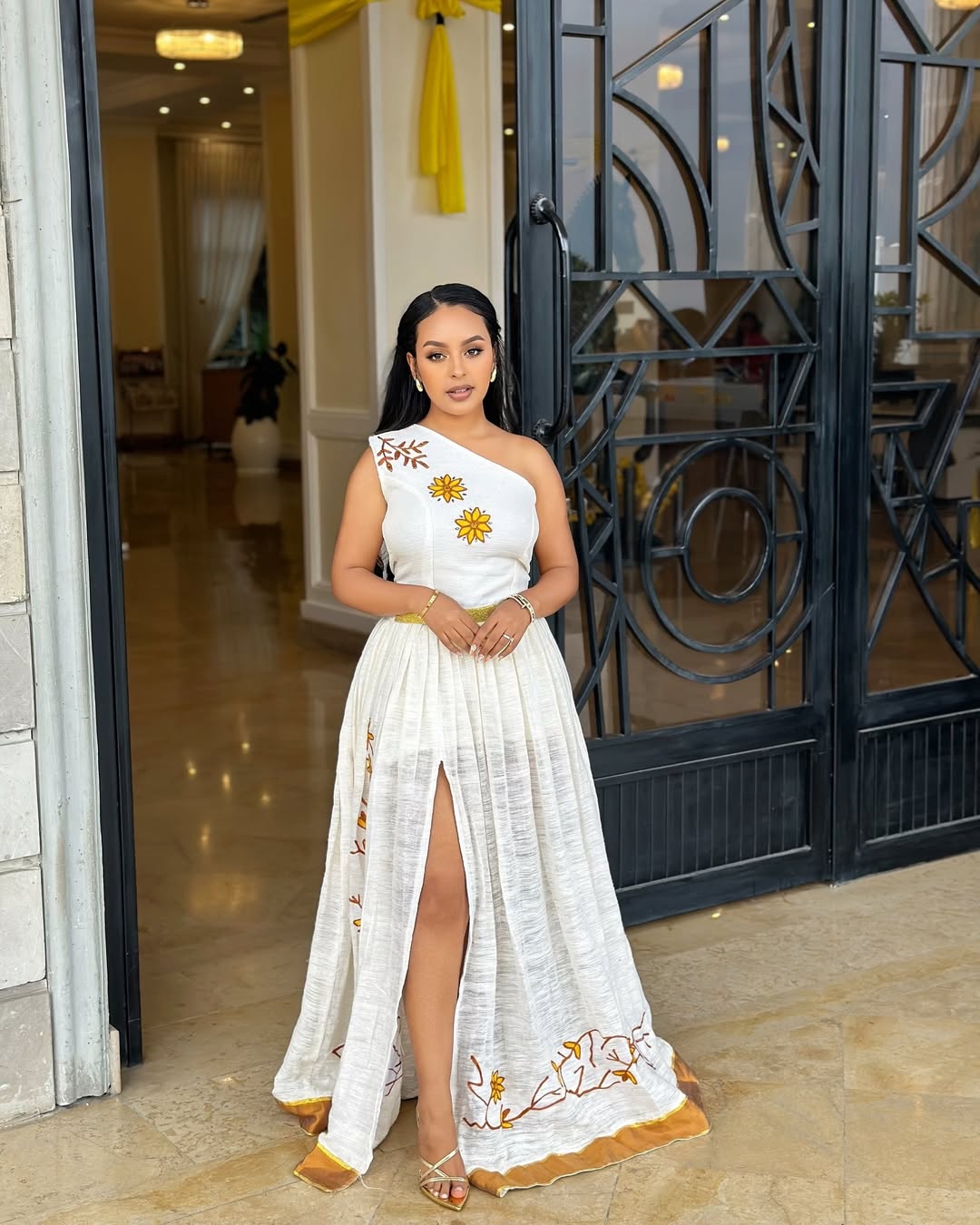 Woman in a white dress with floral patterns standing in a doorway.