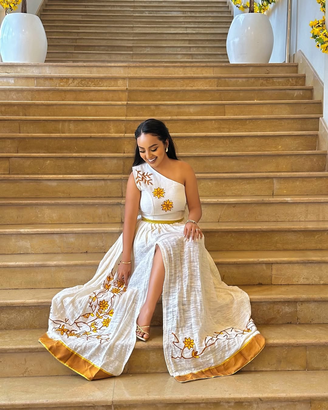 Woman in a white dress with gold embroidery sitting on a staircase.