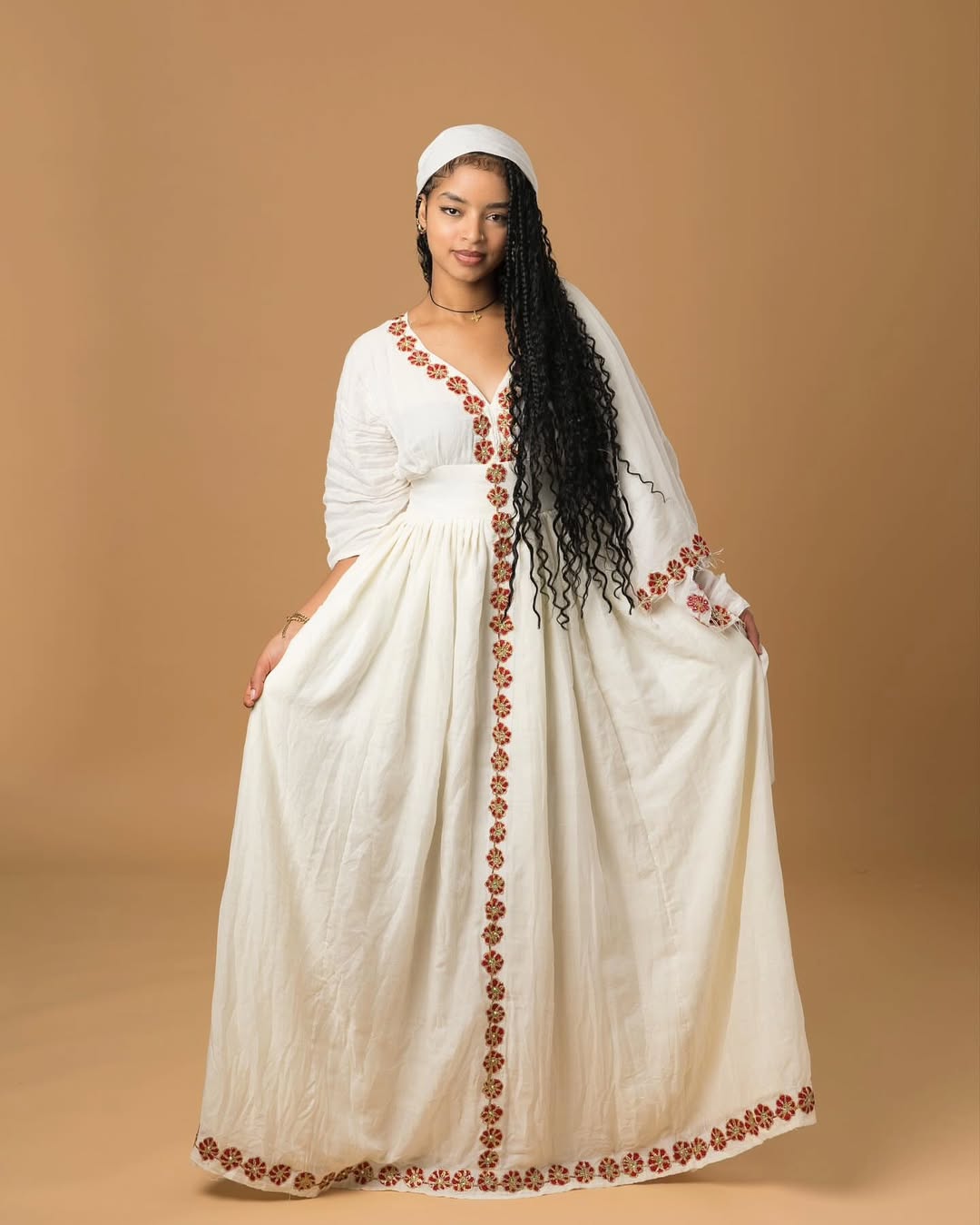 Woman wearing a long, white dress with floral embroidery on a beige background Red Flower Zuria Habesha Kemis Modern Ethiopian Traditional Dress ethgebya simple habesha kemis gebeya