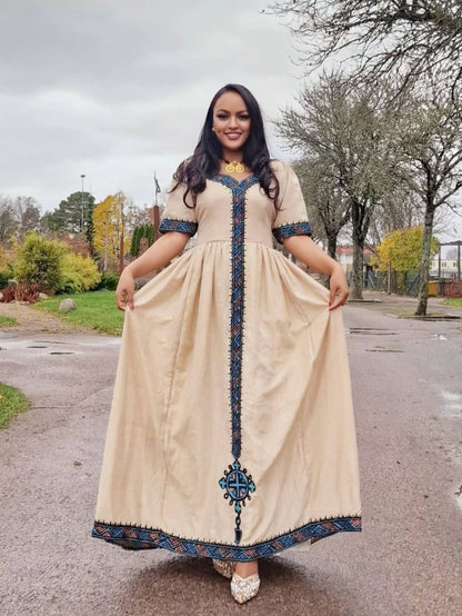 Woman wearing a long, beige dress with blue embroidery standing on a street. Beige Modern Zuria Habesha Kemis Stylish Ethiopian Traditional Dress ethgebya gebeya habesha kemis