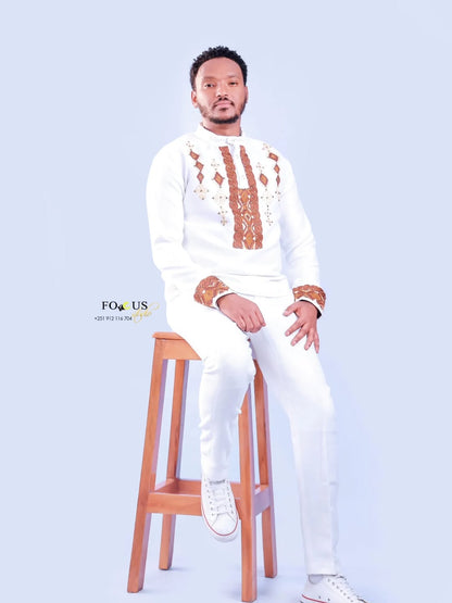 Man in a white outfit with brown patterns sitting on a wooden stool against a light blue background. Ethiopian gown, Habesha wedding dress, Eritrean evening dress, Ethiopian traditional gown, Ethiopian heritage dress, Habesha chic, Eritrean cultural attire, Habesha elegant dress, Eritrean bridal wear, Ethiopian vintage dress, Habesha bridesmaid dress, African ethnic dress, Ethiopian handcrafted dress, Eritrean handcrafted dress, traditional African gown, Habesha festive dress, Ethiopian formal wear,