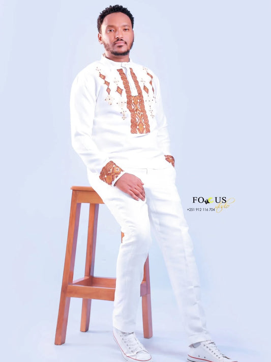 Man in a white outfit with brown patterns standing next to a wooden stool on a light blue background. Ethiopian gown, Habesha wedding dress, Eritrean evening dress, Ethiopian traditional gown, Ethiopian heritage dress, Habesha chic, Eritrean cultural attire, Habesha elegant dress, Eritrean bridal wear, Ethiopian vintage dress, Habesha bridesmaid dress, African ethnic dress, Ethiopian handcrafted dress, Eritrean handcrafted dress, traditional African gown, Habesha festive dress, Ethiopian formal wear,