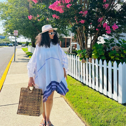 Woman in a white dress with blue trim and straw hat standing on a sidewalk with a white picket fence and pink flowers in the background. modern ethiopian dress habesha traditional dress habesha dress online shopping ethiopian habesha kemis ethiopian kemis habesha libs ethiopian new dress habesha attire fashion ethiopian dress ethiopian women's dress women's ethiopian clothing modern ethiopian traditional clothes habesha cultural dress habesha traditional cloth new ethiopian traditional dress ethiopian tradi