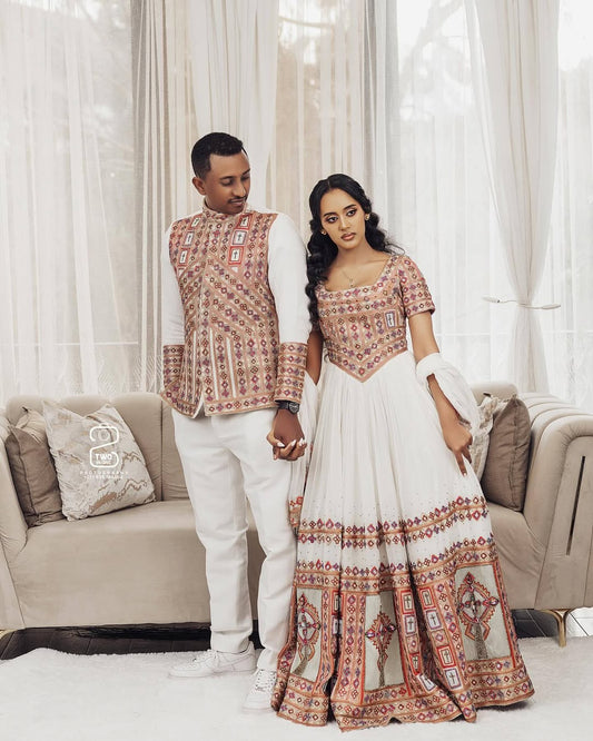Couple in traditional attire standing in a living room with white curtains. Ethiopian Brown Habesha Wedding Attire Matching Couple Set Ethgebya
