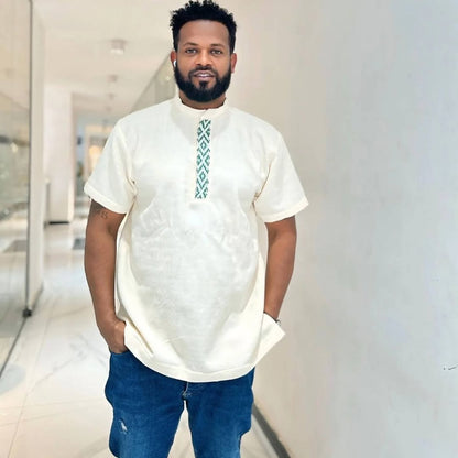 Man wearing a white traditional outfit with blue pants in an indoor setting. Traditional Green Accent Habesha Men’s Cloth Ethiopian Eritrean Attire Ethiopia gebeya