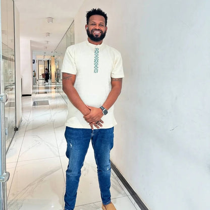 Man in a white shirt and blue jeans standing in a modern hallway. Traditional Green Accent Habesha Men’s Cloth Ethiopian Eritrean Attire Ethiopia gebeya