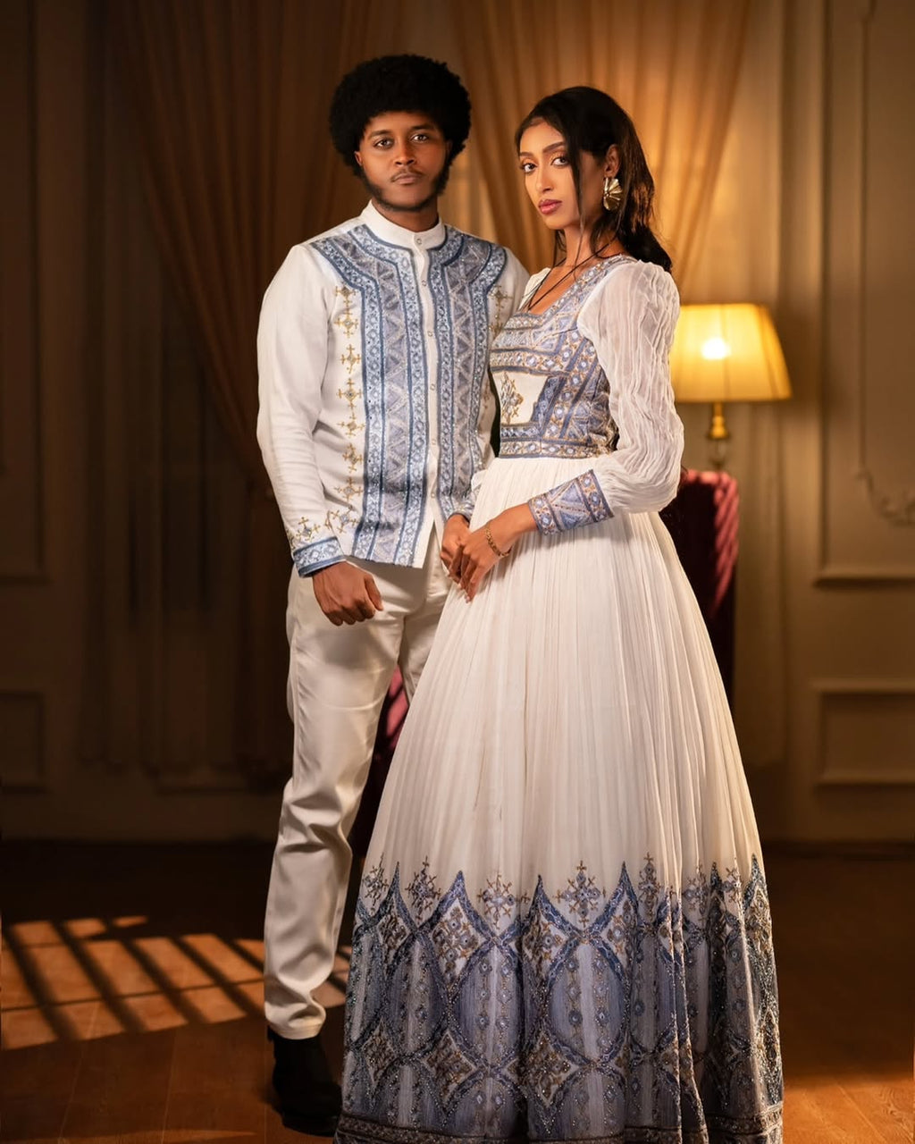 Two people in traditional attire standing in a warmly lit room. Blue Habesha Couple Outfit New Elegant Matching Ethiopian Attire ethgebya gebeya fikregna fiqregnoch