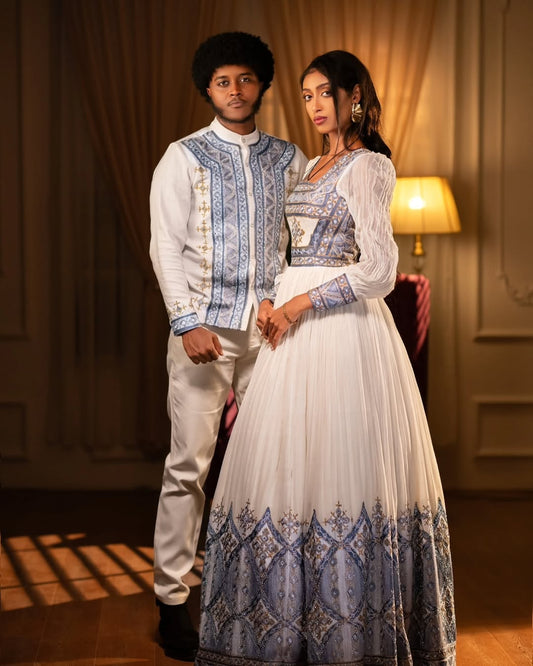 Two people in traditional attire standing in a warmly lit room. Blue Habesha Couple Outfit New Elegant Matching Ethiopian Attire ethgebya gebeya fikregna fiqregnoch