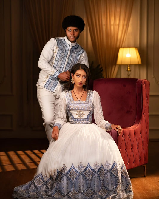 Two people in formal attire sitting on a red armchair in a dimly lit room. Blue Habesha Couple Outfit New Elegant Matching Ethiopian Attire ethgebya gebeya fikregna fiqregnoch