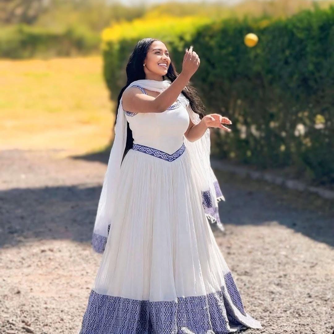 White Flowy Traditional Habesha kemis, Eritrean & Ethiopian Cultural Dress featuring Blue Embroidery Along The Hem.