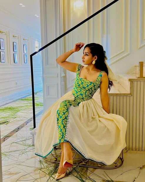 Woman in a green and white traditional outfit sitting on a chair in an elegant interior setting.