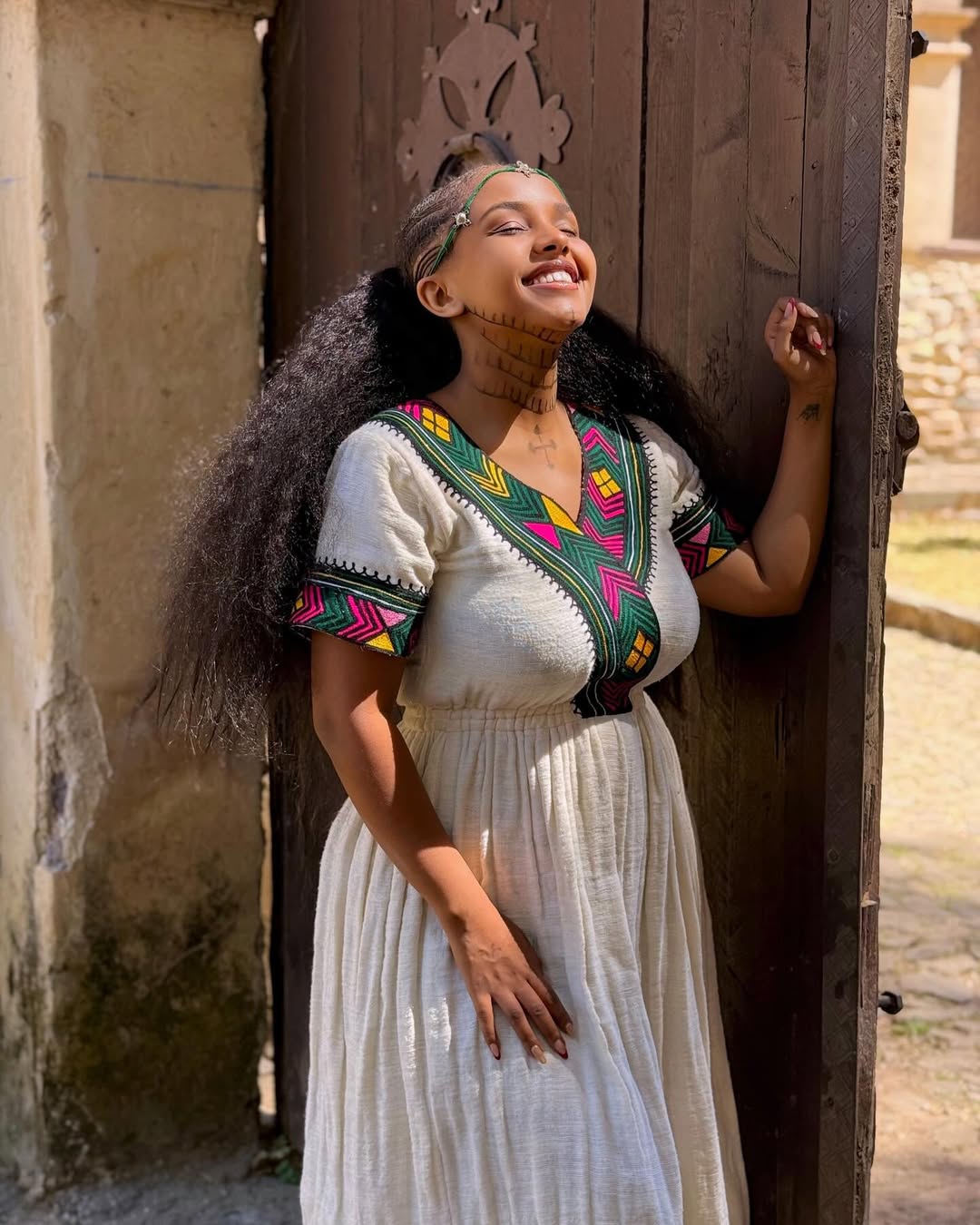 Woman in traditional attire standing against a wooden door  Multicolor Gondar Habesha Kemis Modern Ethiopian Traditional Dress ethgebya gebeya
