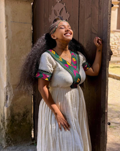 Woman in traditional attire standing against a wooden door  Multicolor Gondar Habesha Kemis Modern Ethiopian Traditional Dress ethgebya gebeya