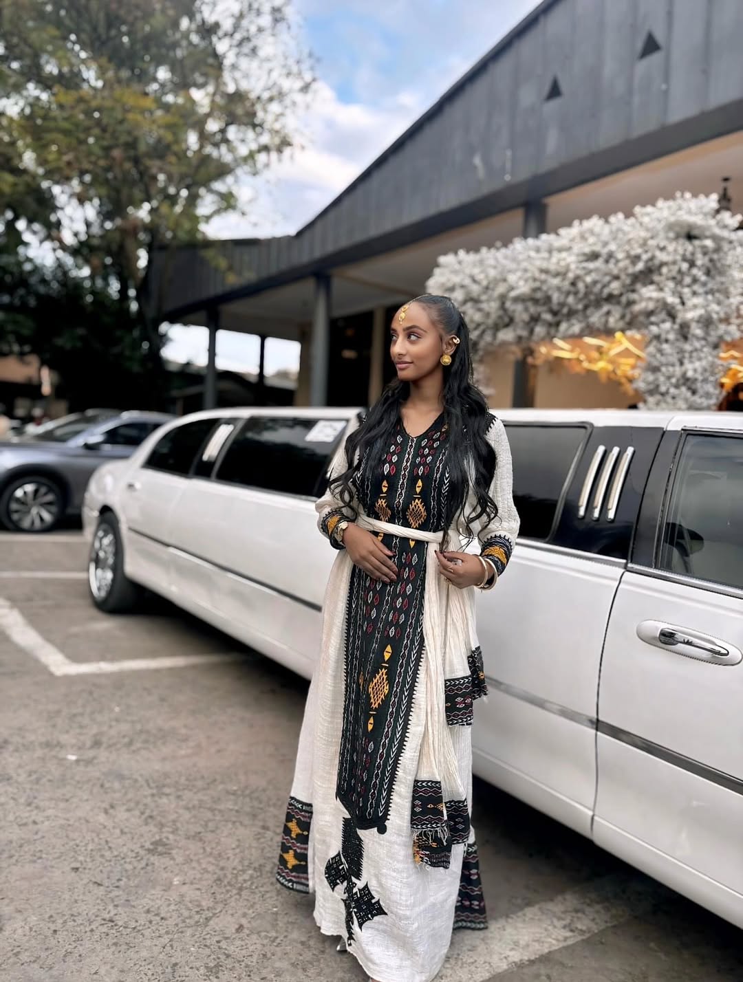Woman in traditional attire standing next to a white limousine in an outdoor setting. Special Axum Habesha Kemis | Modern Ethiopian Traditional Dress
