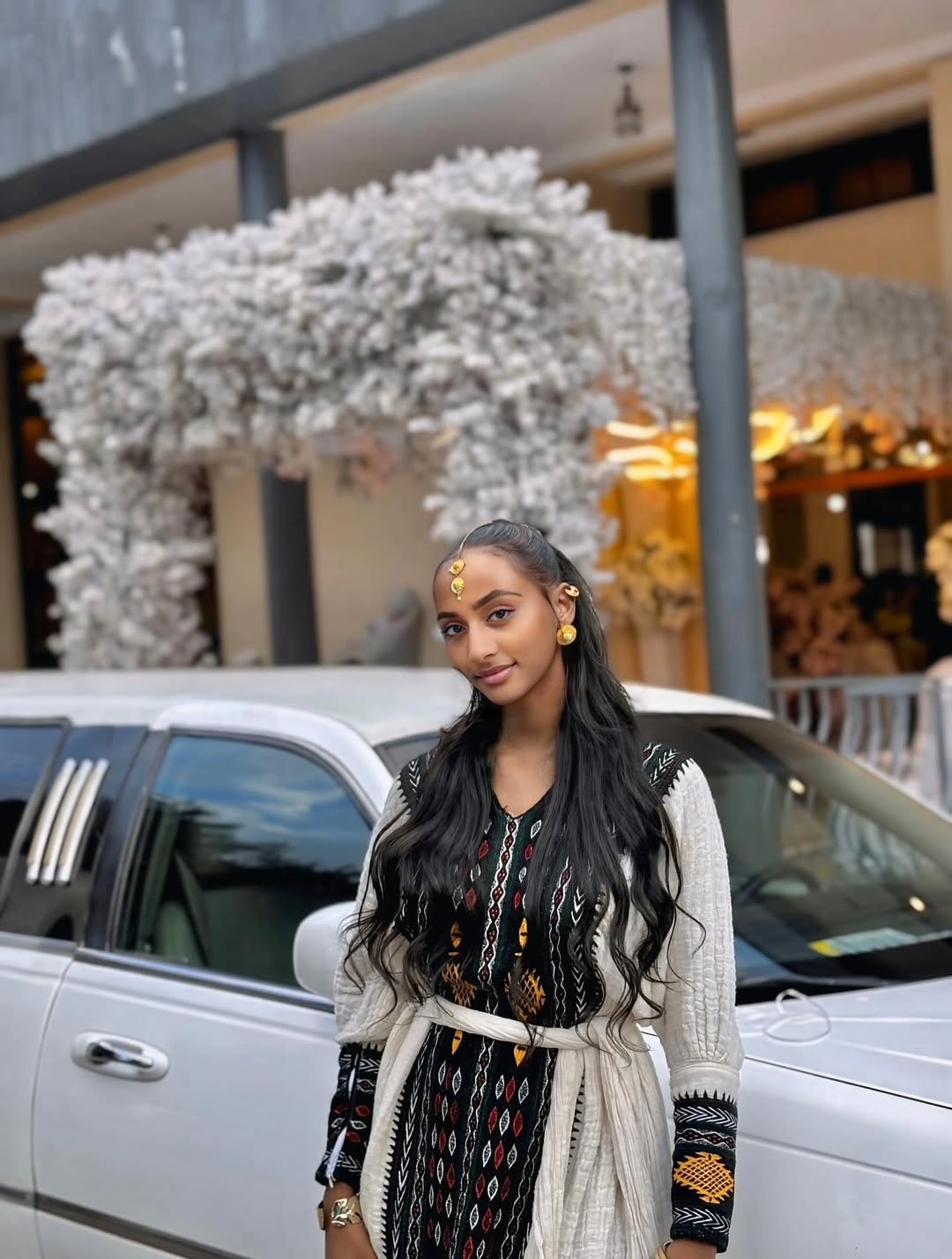 Woman standing in front of a white car with decorative flowers in the background Special Axum Habesha Kemis | Modern Ethiopian Traditional Dress