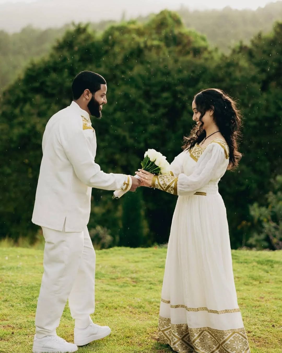 Man and woman in formal attire standing on grass with trees in the background.  Golden Habesha Couple Outfit Modern Ethiopian Matching Set ethgebya gebeya