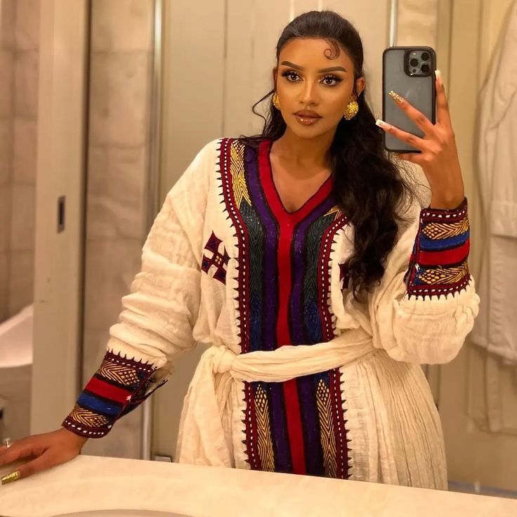Woman taking a mirror selfie wearing a colorful dress with intricate  Elegant Ethiopian & Eritrean Axum Habesha Dress Ethgebyapatterns.