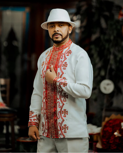 Man wearing a white hat and a traditional embroidered shirt with red patterns in an indoor setting. ethiopian and eritrean mens traditional wear ethgebya