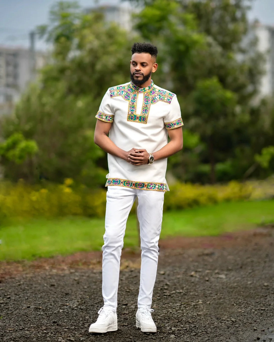 Man wearing a traditional outfit with colorful embroidery in an outdoor setting Men’s Short Sleeve Habesha Shirt White Ethiopian Traditional Wear ethgebya
