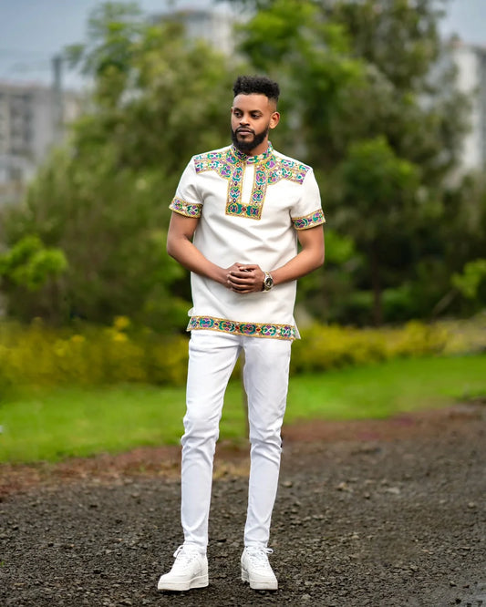 Man wearing a traditional outfit with colorful embroidery in an outdoor setting Men’s Short Sleeve Habesha Shirt White Ethiopian Traditional Wear ethgebya