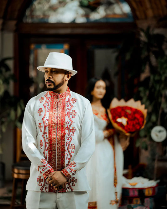 Man in traditional embroidered outfit with a blurred woman in the background. ethiopian and eritrean mens traditional wear ethgebya