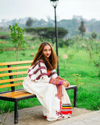 Woman sitting on a bench in a park with greenery and a lamp post in the background gondar habesha kemis ethgebya