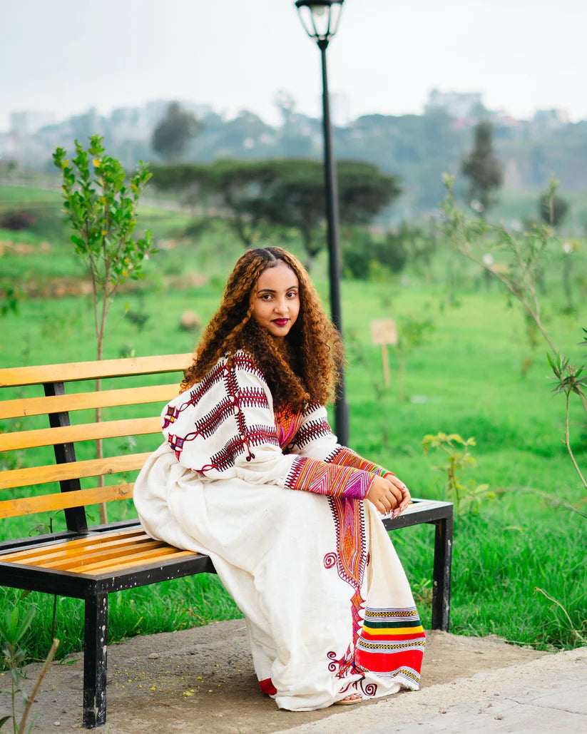 Woman sitting on a bench in a park with greenery and a lamp post in the background gondar habesha kemis ethgebya