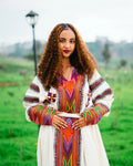 Woman wearing a colorful traditional outfit in a green outdoor setting. gondar habesha kemis ethgebya