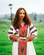 Woman wearing a colorful traditional outfit in a green outdoor setting. gondar habesha kemis ethgebya