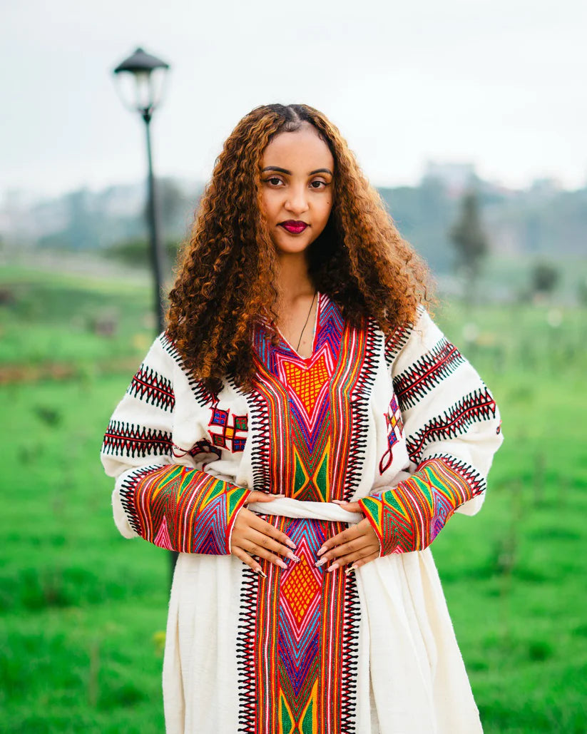 Woman wearing a colorful traditional outfit in a green outdoor setting. gondar habesha kemis ethgebya