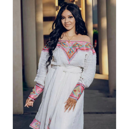 Woman wearing a white dress with colorful embroidery standing outdoors.