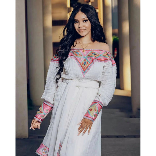 Woman wearing a white dress with colorful embroidery standing outdoors.