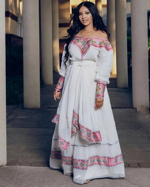 Woman in a white and pink traditional outfit standing in front of columns.