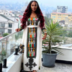 Woman in a colorful dress standing on a balcony with a cityscape background