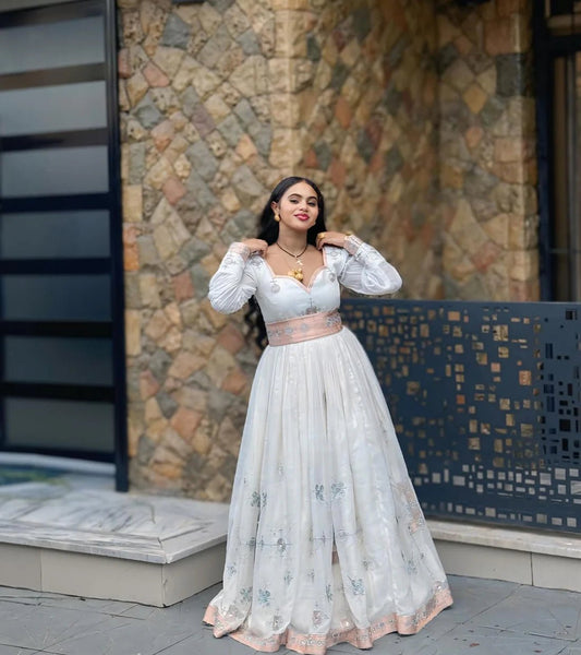 Woman in a white floral dress standing against a stone wall.