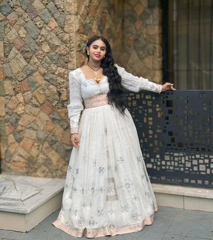Woman in a white and pink traditional outfit standing against a stone wall.