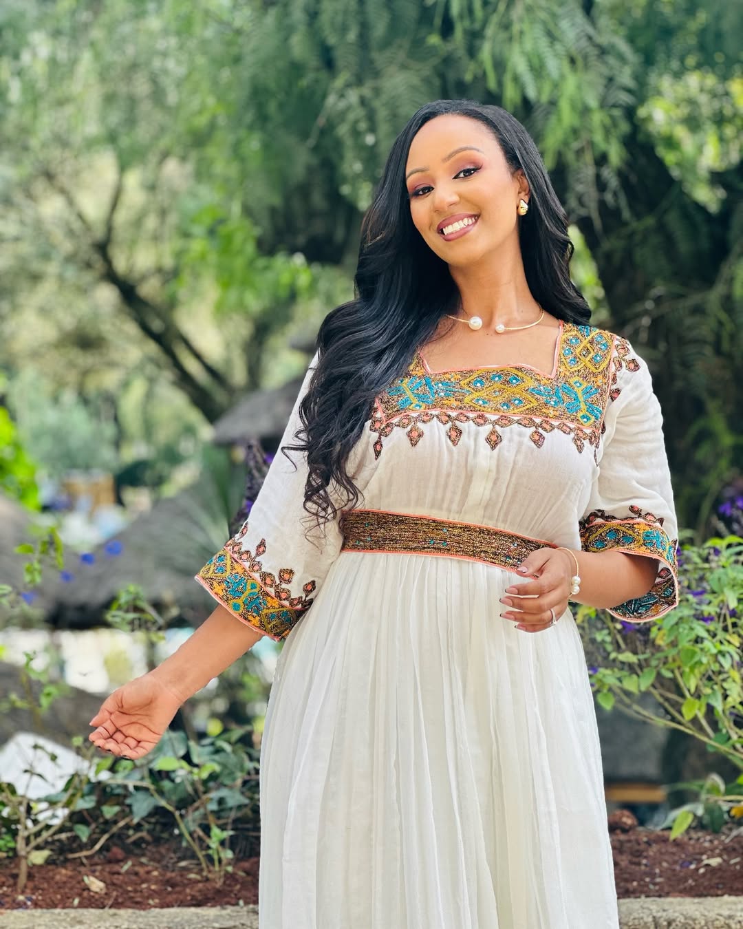 Woman in a white dress with colorful embroidery standing outdoors.  Light Green & Gold Zuria Habesha Kemis Ethgebya