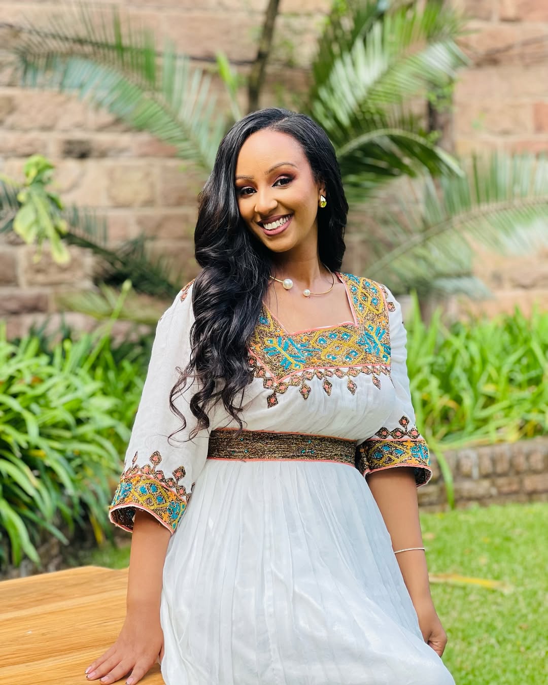 Woman in a traditional outfit with floral patterns standing outdoors in a garden.  Light Green & Gold Zuria Habesha Kemis Ethgebya