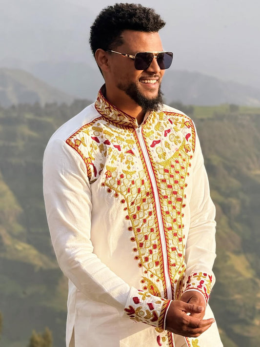 Man wearing a traditional embroidered outfit with sunglasses against a mountainous background Red & Gold Habesha Men's Shirt Ethgebya