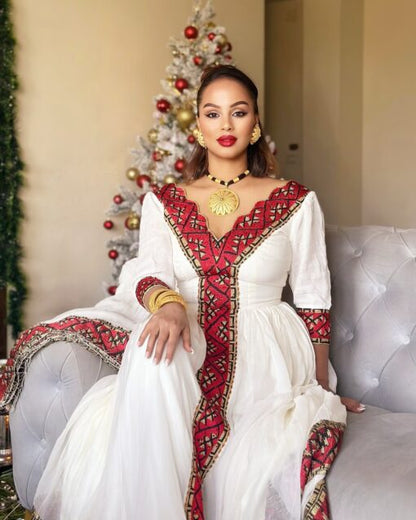 Woman in a white and red traditional outfit sitting on a couch with a decorated Christmas tree in the background.